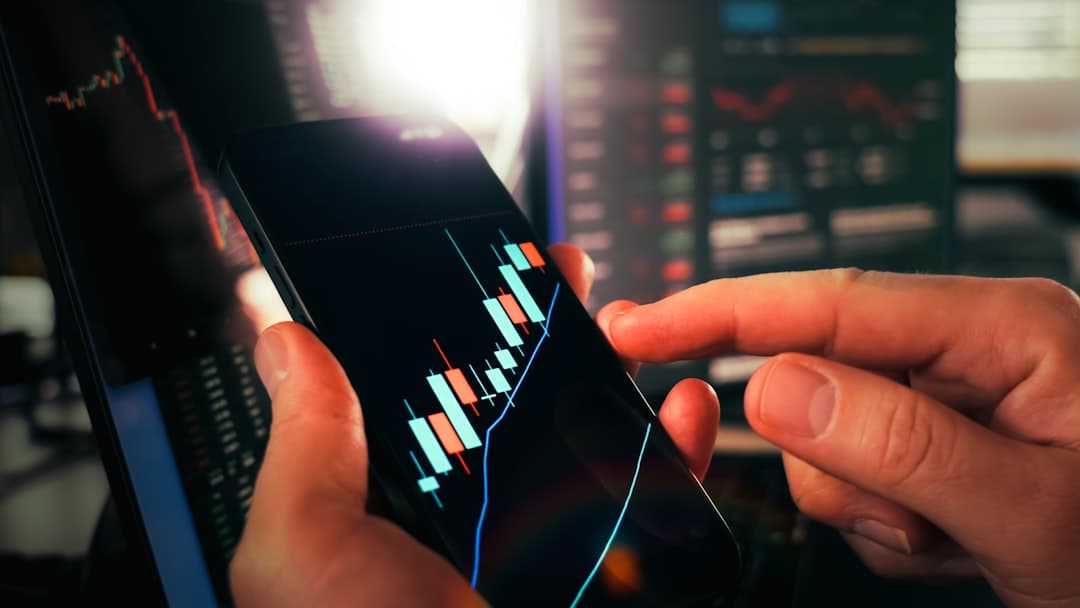 Compound Interest Explained: How Money Multiplies — Hands holding smartphone showing stock market data